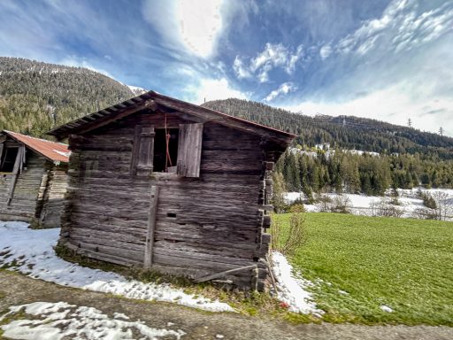 Alte Holzhütte auf grüner Wiese vor alpiner Landschaft