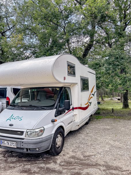 Wohnmobil auf einem Campingplatz, umgeben von Bäumen.
