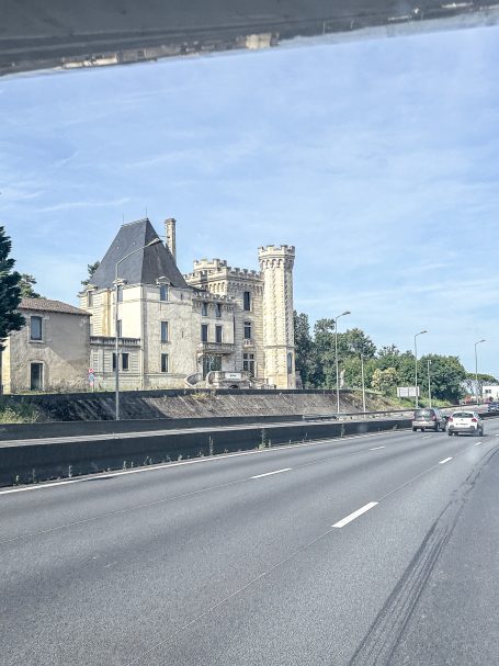Historisches Gebäude mit Türmen neben einer Autobahn unter klarem Himmel.