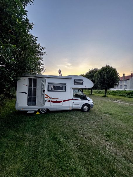 Wohnmobil auf einer Wiese bei Sonnenuntergang, umgeben von Bäumen.