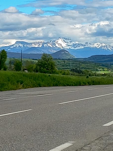Ein Blick auf die französischen Alpen Schneebedeckte Berge hinter Straße und grünen Wiesen