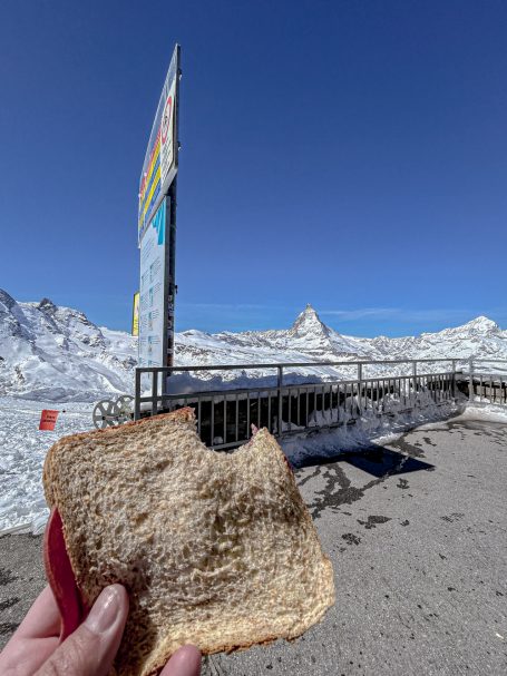 Brotzeit mit Aussicht Hand hält Brot vor verschneiter Berglandschaft
