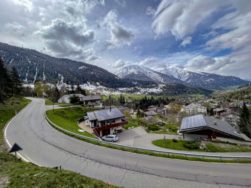 Alpendorf mit kurviger Straße und Bergen im Hintergrund