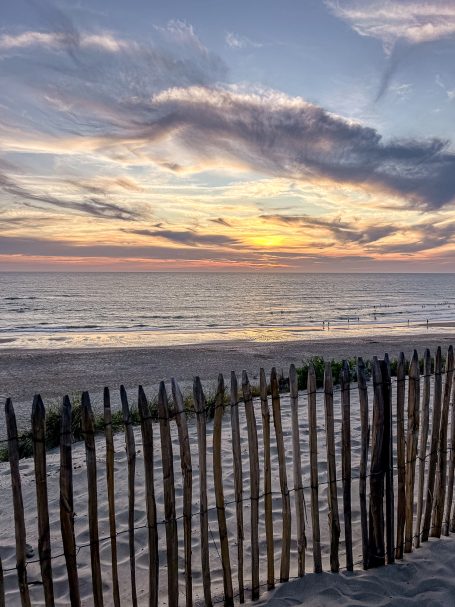 Sonnenuntergang über dem Meer, Blick durch einen Holzzaun auf den Strand.