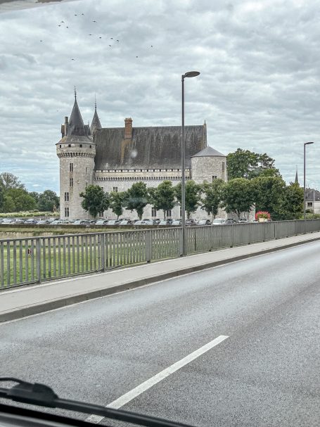 Historisches Gebäude mit Türmen und Grünanlagen, an einer Straße gelegen.