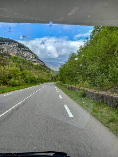 Straße durch ein bewaldetes Tal mit Bergen im Hintergrund