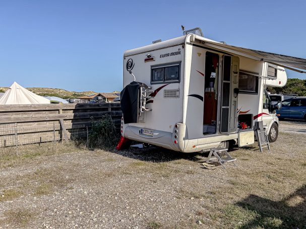 Wohnmobil steht auf einem gepflasterten Platz, umgeben von niedrigen Zäunen und Gras.