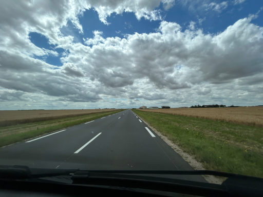 Gerade Straße durch offene Felder unter wolkenreichem Himmel