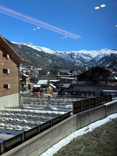 Alpendorf mit Häusern und Bergen unter blauem Himmel