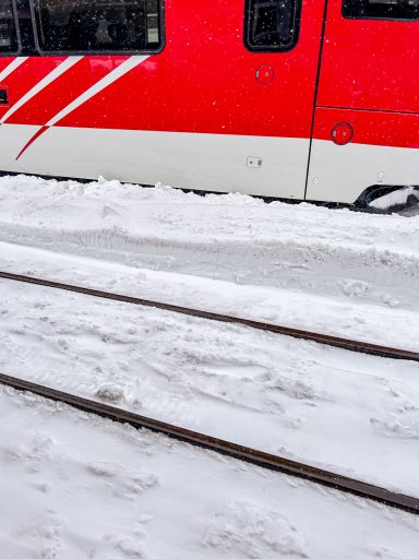 Zugschienen im Schnee neben einem roten Zug