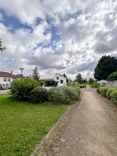 Weg mit grünen Pflanzen und einem Gebäude im Hintergrund unter bewölktem Himmel.